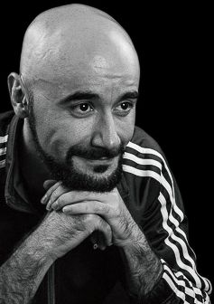 Picture of Pedro Rodrigues (Treze413) in black and white, he is gently smiling while looking in south east direction while gently resting his chin on his hands, in this picture he looks bald and has facial hair